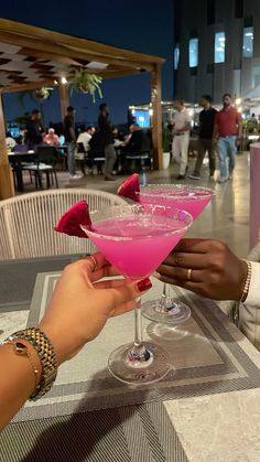 two people holding up pink drinks at a table