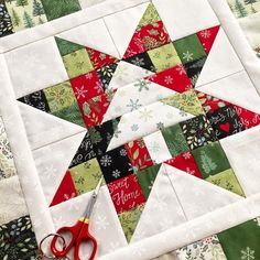 a quilted table topper with scissors next to it and christmas decorations in the background