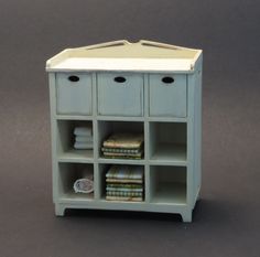 a white shelf with several drawers and books on it's sides, sitting on a gray surface