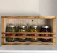 an open wooden shelf with jars and pickles in it on top of a white mantle