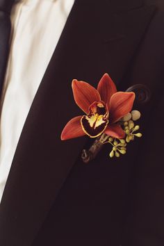 a red flower is attached to the lapel of a black suit