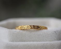 a yellow gold wedding band with leaves on the side, sitting on top of a white cloth