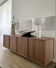 an open book on top of a wooden cabinet next to a vase with flowers in it