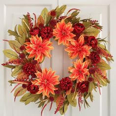 an orange wreath with red flowers and green leaves on a white front door, decorated with greenery