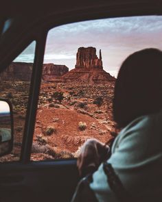 a person sitting in a car looking out the window at an area with rocks and mountains