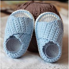 two crocheted baby shoes sitting on top of a bed next to a ball of yarn