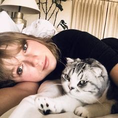 a woman laying on top of a bed next to a gray and white cat in her lap