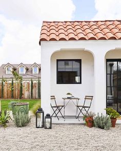 a small white house with a table and chairs in the front yard, surrounded by potted plants