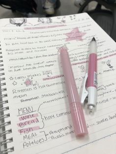 two pink pens sitting on top of a notebook next to an empty pen and paper