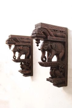 two carved wooden elephants on shelves against a white wall