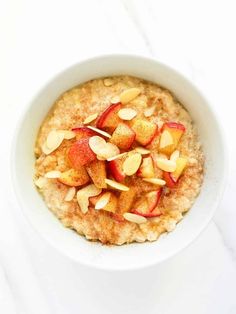 a bowl of oatmeal with apples and almonds in it on a white table