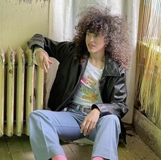 a woman with curly hair sitting on the floor next to a radiator and heater