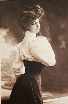 an old fashion photo of a woman in a long dress with her hands on her hips