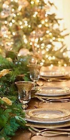 the table is set with gold plates and place settings in front of a christmas tree