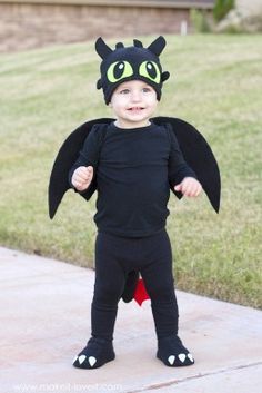 a little boy dressed up in a black costume with green eyes and a dragon hat