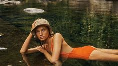 a woman in an orange swimsuit and hat laying on the ground next to water