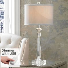 a glass table lamp sitting on top of a white chair in front of a window