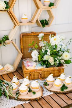 some cupcakes are sitting on trays next to a basket with flowers and greenery