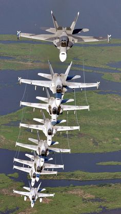 four planes flying in formation over the water and land area with grass on both sides