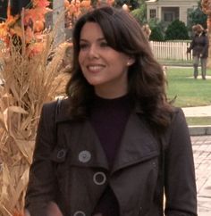 a woman standing next to a tall plant in front of a white fence and house