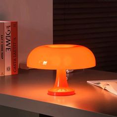 an orange table lamp sitting on top of a desk next to a bookshelf