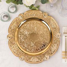 a gold plate sitting on top of a white table next to silverware and flowers