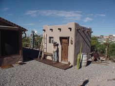 a man standing in front of a small adobe style building with a ladder to the door