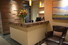 a brown chair sitting in front of a counter with flowers on it and a painting behind it