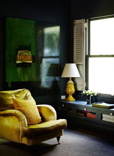 a yellow chair sitting in front of a window next to a table with a lamp on it