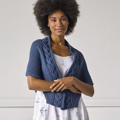 a woman standing with her arms crossed wearing a blue knitted cardigan and white dress