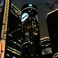 two tall buildings lit up at night with the moon in the sky above them and one building has a batman logo on it