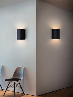 two chairs sitting next to each other in front of a white wall with black lamps on it