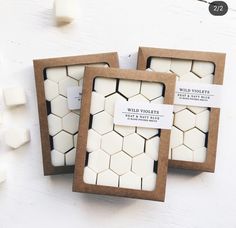 three small white candles in wooden boxes with labels on them