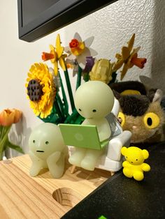 two little figurines sitting on top of a table next to flowers and a laptop