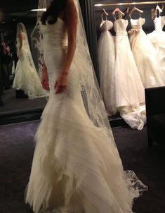 a woman standing in front of a mirror wearing a wedding dress