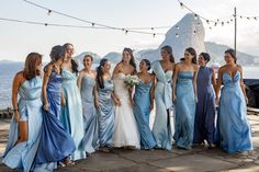 a group of women standing next to each other near the ocean with string lights strung over them