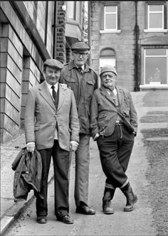 three men standing next to each other in front of a brick building on a city street