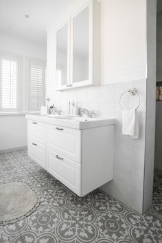 a white bathroom with grey and white tile flooring on the shower wall, sink vanity and mirror