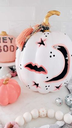 a white pumpkin with black and pink designs on it, sitting next to other decorations