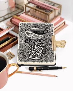 an open notebook sitting on top of a desk next to a cup of coffee and pencils