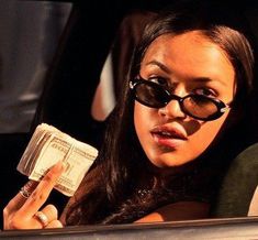 a woman sitting in the back seat of a car holding money and wearing black sunglasses