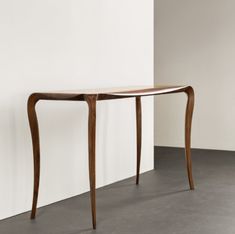 a wooden table sitting on top of a floor next to a white wall in an empty room