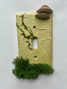 a decorative light switch cover with moss growing on it and a mushroom sitting on top