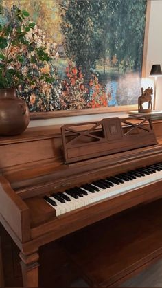 a piano sitting in front of a painting on the wall next to a vase with flowers