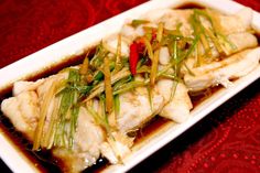 a white plate topped with fish covered in sauce and green onions on top of a red table