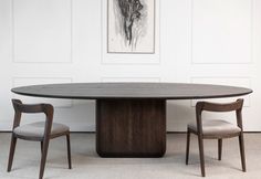 an oval table with two chairs around it in front of a white paneled wall