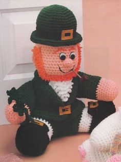 a crocheted st patrick's day doll sitting next to a teddy bear