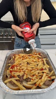 a woman holding a container of food in front of a pan filled with french fries