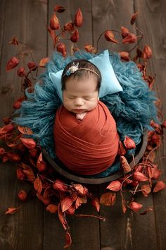 a newborn baby wrapped in a blue blanket and wearing a red shirt is sitting on a wooden floor