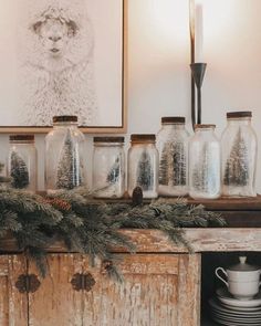 there are many glass jars on the mantle with pine branches in front of them and one is empty